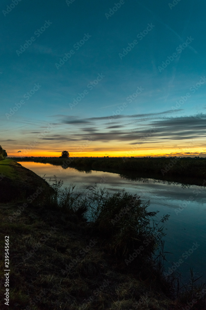 Twilight sky over a river in Holland. Beautiful colors in the sky and reflections in the calm water. Photographed between the cities of Gouda and Leiden in The Netherlands.