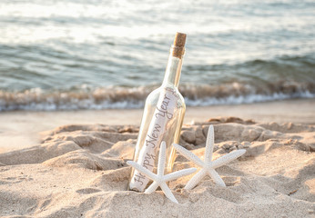 Happy New Year message in a bottle with pair of white starfish in beach sand and ocean water background