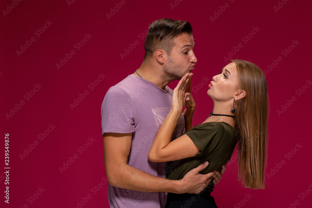 Portrait of outraged displeased woman gesturing to stop with hand while man trying to kiss her on burgundy background Portrait of outraged displeased woman gesturing to stop with hand while man trying to kiss her on burgundy background