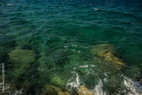 vivid blue and green sea water surface with waves and drops, transparent view to stone bottom