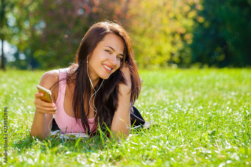 Young woman in dress lies on green grass and listens to music in headphones through smartphone. Young woman in dress lies on green grass and listens to music in headphones through smartphone.