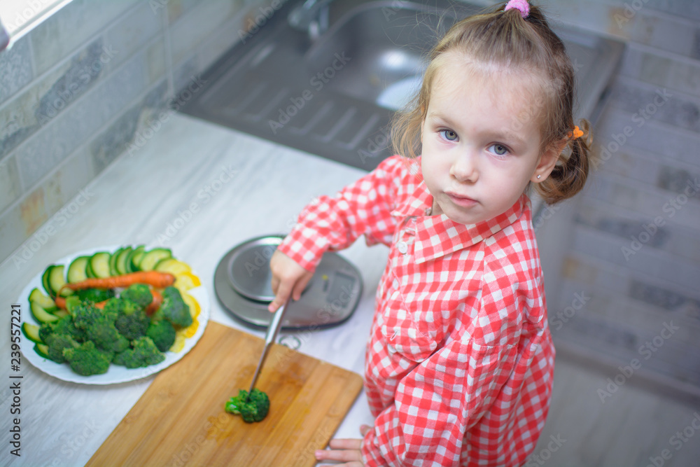 Cute baby girl in shirt is cutting with a knife vegetables cabbage