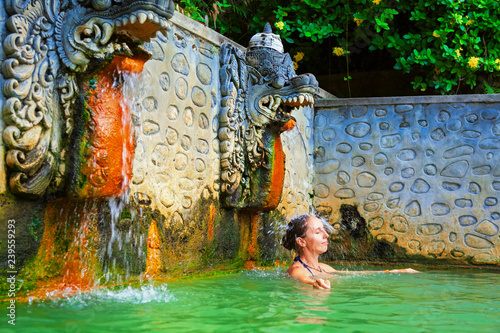 Young woman stand in thermal bath, relaxing under flowing water stream of shower in natural mineral hot spring Banjar. Day tour on family holidays. Popular travel destination, traditional spa in Bali photo