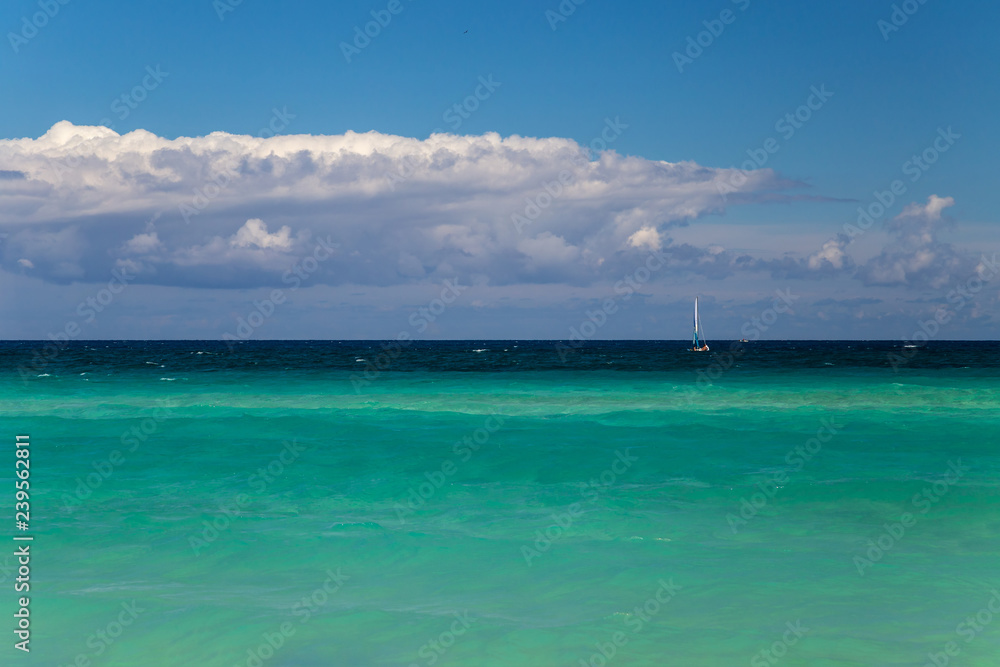 Background of turquoise sea, sky and clouds. Small sailboat at the horizon