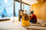 Young couple dressed in bright sweaters sitting near the fireplace in the modern house in the mountains durnig winter time