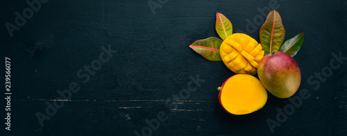 Fototapeta Mango z liśćmi na czarnym drewnianym tle. Owoce tropikalne. Widok z góry. wolne miejsce na Twój tekst.