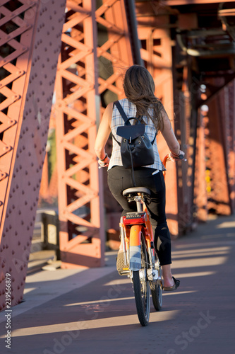 Fototapeta Naklejka Na Ścianę i Meble -  Slender girl with backpack rides bicycle on drawbridge