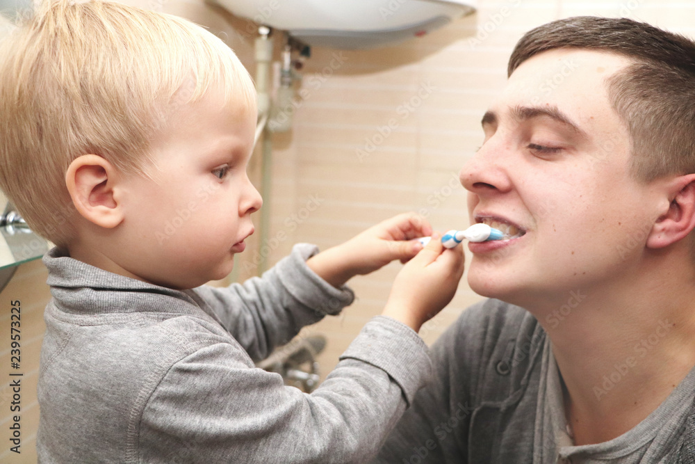 Dad and son brush their teeth in the bathroom. Father Brushing Teeth to Child Dad and son brush their teeth in the bathroom. Father Brushing Teeth to Child
