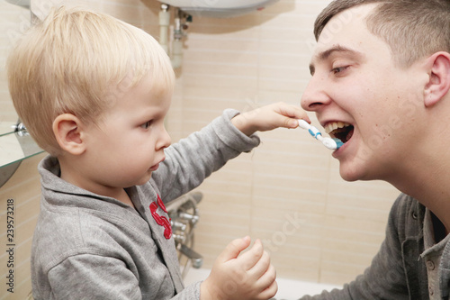 Dad and son brush their teeth in the bathroom. Father Brushing Teeth to Child