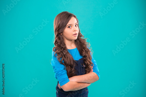 Girl curly hairstyle feels confident. Child hold hands confidently crossed chest. Child psychology and development. Confident posture. Upbringing confidence. Kid girl long hair posing confidently © be free
