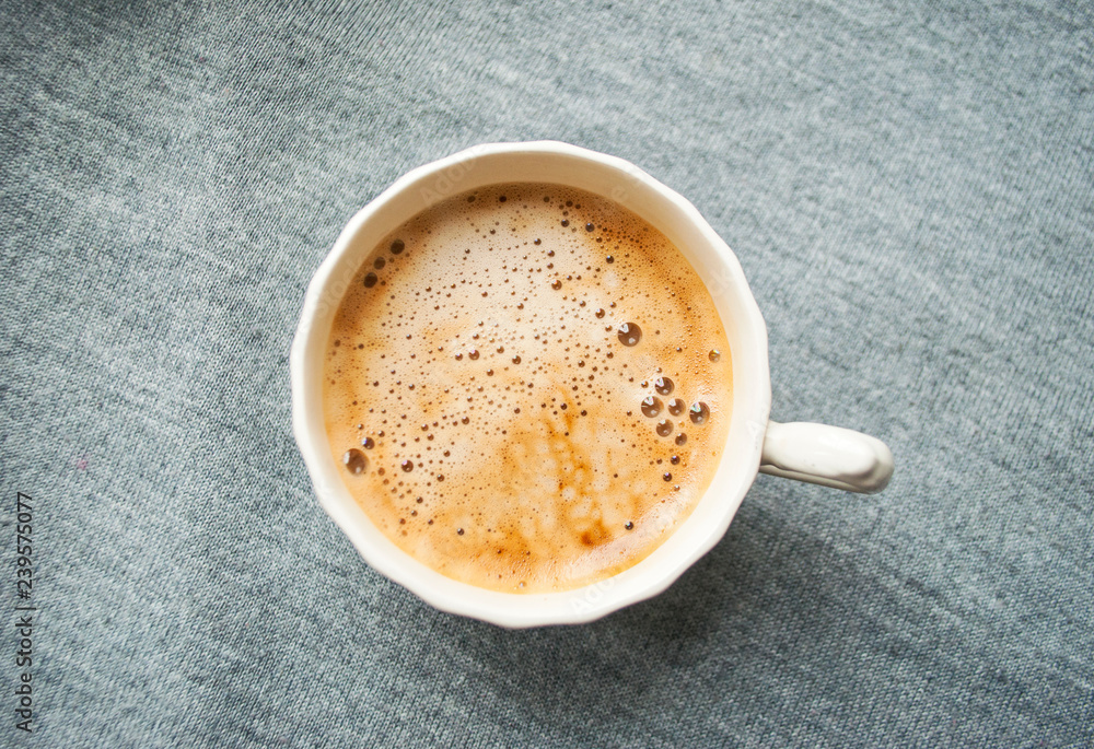 A cup of fresh coffee with beautiful foam on grey background. Flat lay style. A cup of fresh coffee with beautiful foam on grey background. Flat lay style.