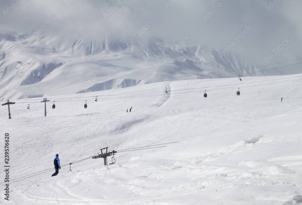 Snowboarder descend on snowy ski slope and high mountains in dark cloud Snowboarder descend on snowy ski slope and high mountains in dark cloud