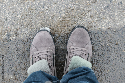 Feet in winter boots made of natural suede and fur on wet asphal