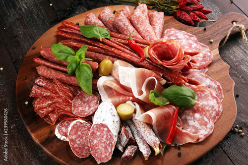 Food tray with delicious salami, pieces of sliced prosciutto crudo, sausage and basil. Meat platter with selection