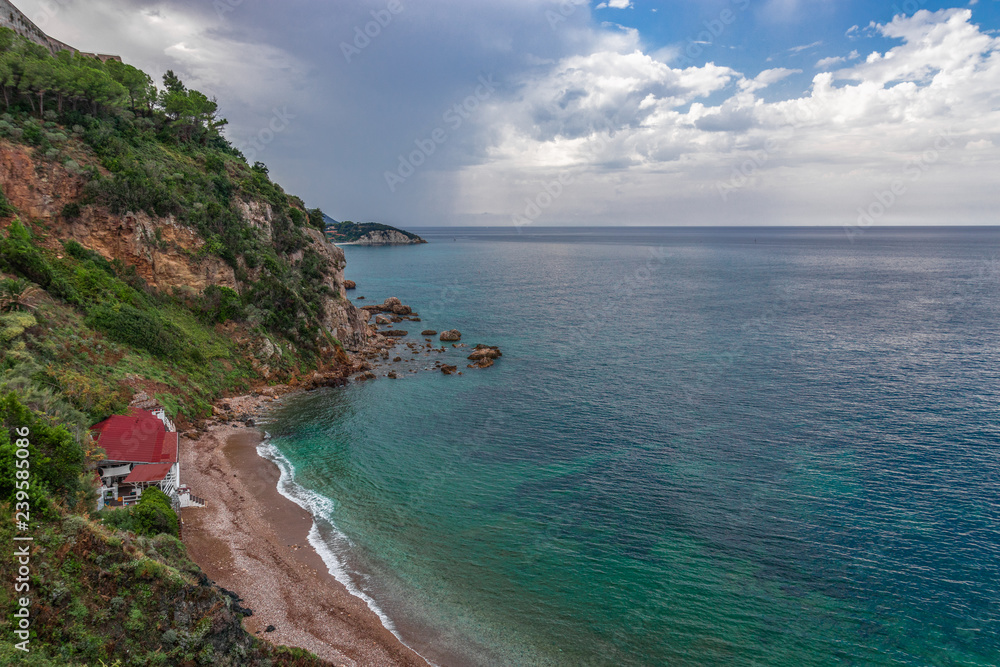 Beautiful seascape of the rocky coast and a small beach with a restaurant. Cloudy sky after rain and emerald waters of the sea of Elba island. Tuscany, Italy