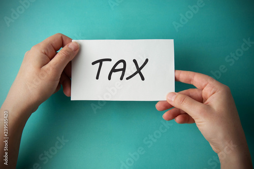 TAX inscription. Woman holding paper with TAX lettering in hands isolated on blue background. Register of taxpayers for property.