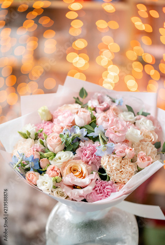 Fototapeta Naklejka Na Ścianę i Meble -  Bright bouquet of mixed flowers. Floral Bunch with blue Delphinium in glass vase. Garland bokeh on background. Christmas love