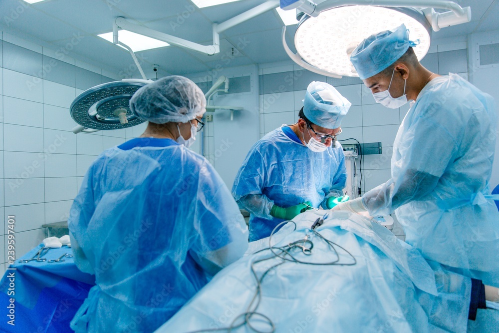 Three in scrubs performing surgery in the operating room Three in scrubs performing surgery in the operating room