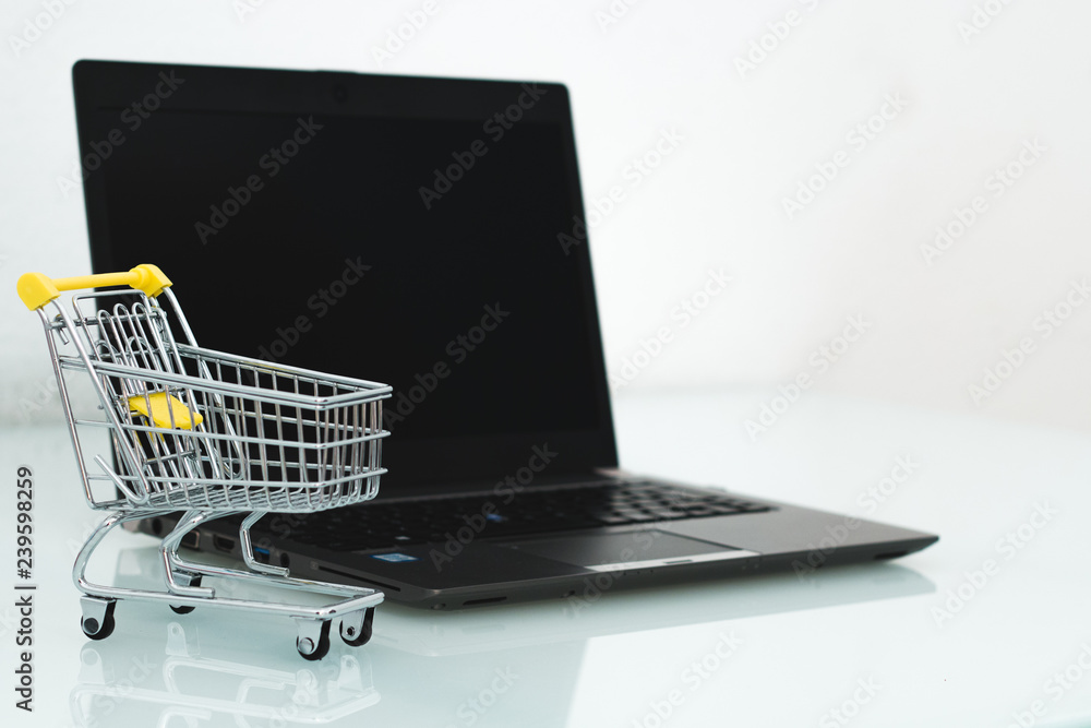 E-commerce concept and shopping online idea. Black computer with a small trolley with white background. Space for text.