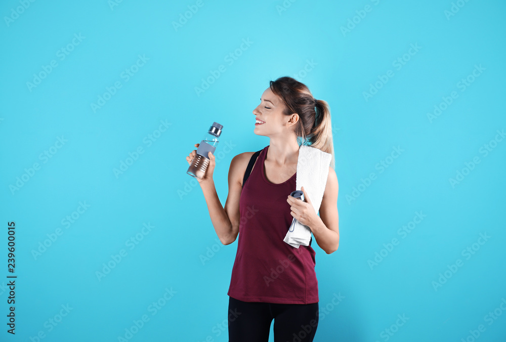 Beautiful young woman in sportswear with towel and bottle of water on color background Beautiful young woman in sportswear with towel and bottle of water on color background