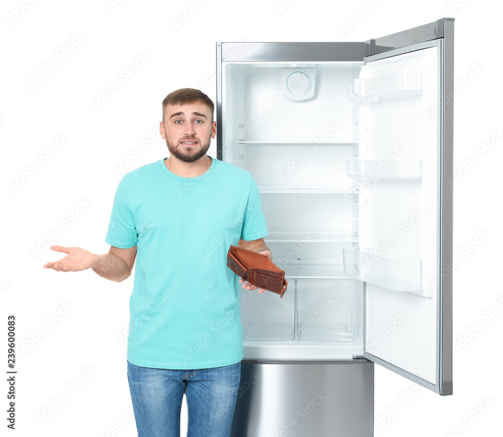 Young man with no money in wallet near empty refrigerator on white background Young man with no money in wallet near empty refrigerator on white background