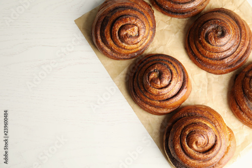Parchment with cinnamon rolls on white wooden background, top view. Space for text