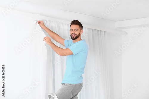 Young handsome man hanging window curtain in room