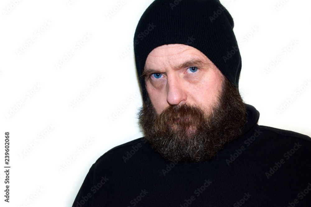 A bearded and mustached man in a black hat looks stern and angry. The descendant of the Vikings. Isolate on white background. A bearded and mustached man in a black hat looks stern and angry. The descendant of the Vikings. Isolate on white background.