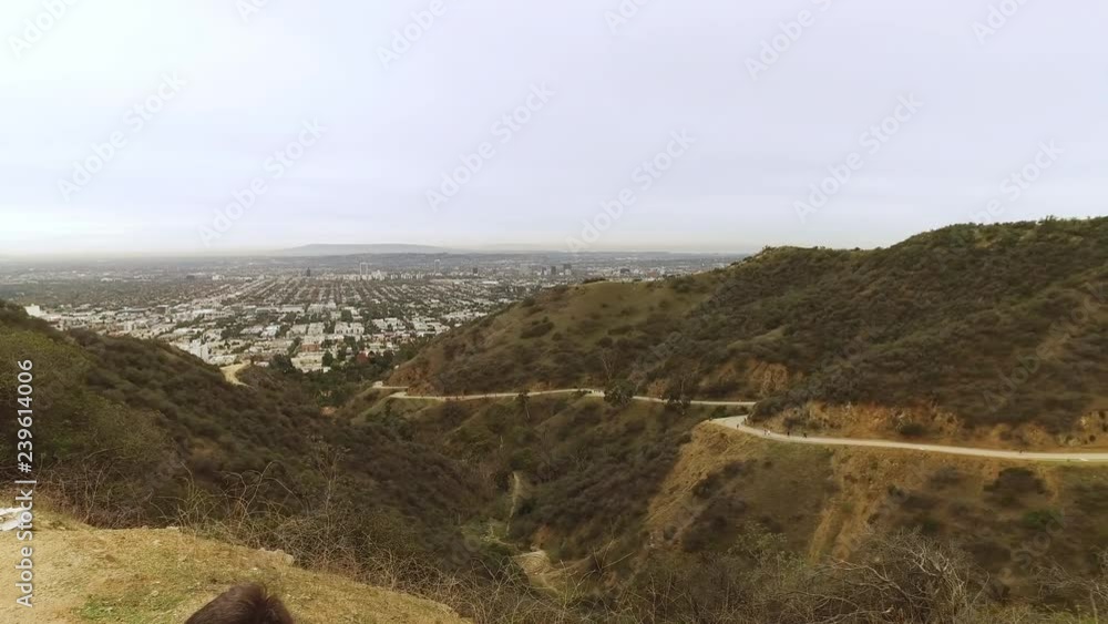 A dolly up shot behind a sitting hiker revealing Runyon Canyon on an overcast day. Hikers on the trail in the distance. A dolly up shot behind a sitting hiker revealing Runyon Canyon on an overcast day. Hikers on the trail in the distance.