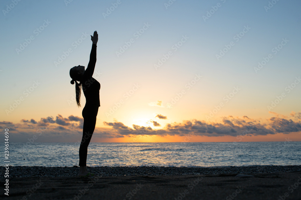 silhouette of woman doing greeting to the sun on the beach at sunrise