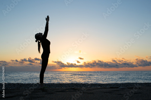 silhouette of woman doing greeting to the sun on the beach at sunrise