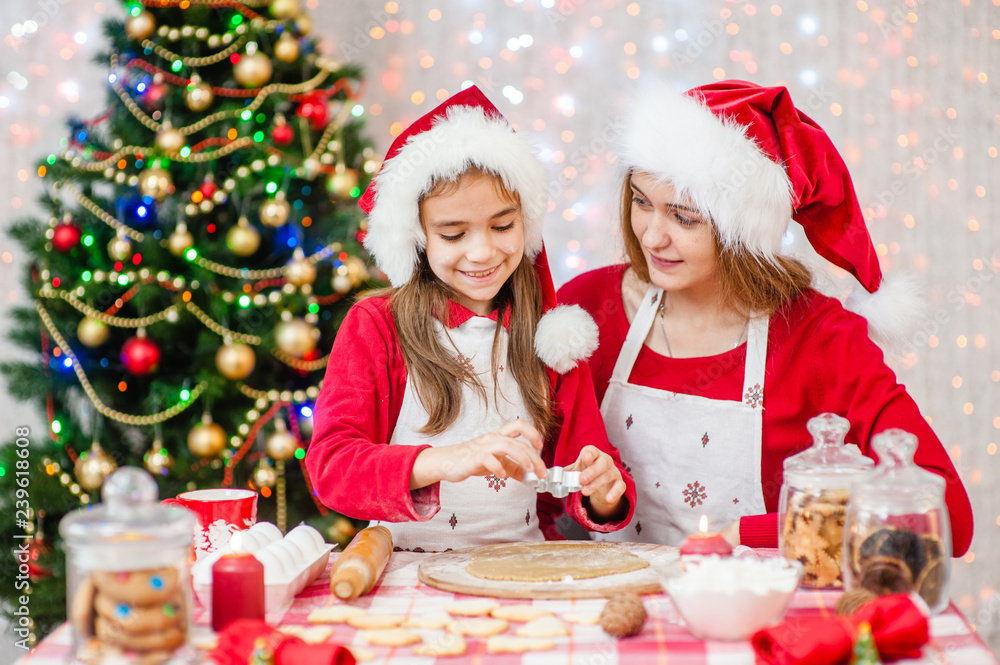 Merry Christmas and Happy Holidays. Mom and daughter in a Christmas hat are preparing a festive treat Merry Christmas and Happy Holidays. Mom and daughter in a Christmas hat are preparing a festive treat