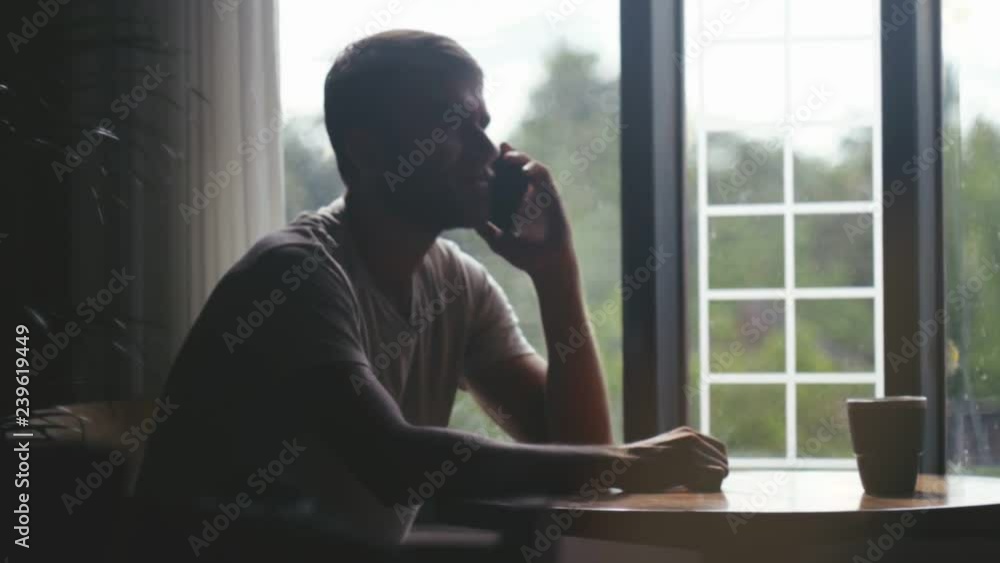 Young unhappy man sitting in cafe and talking on mobile phone