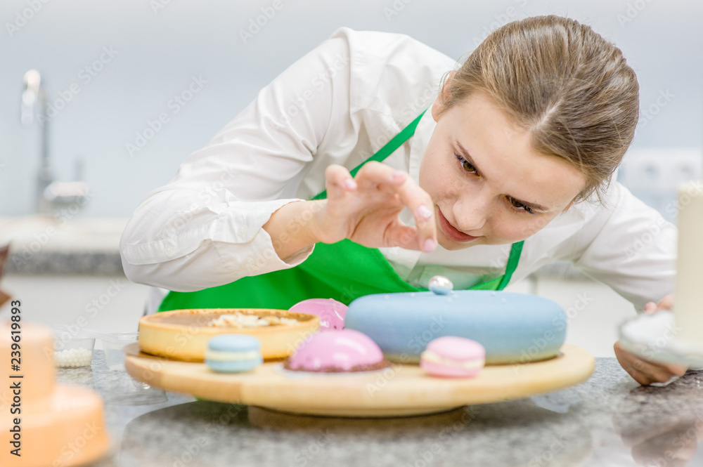 Young confectioner decorating  cake at kitchen