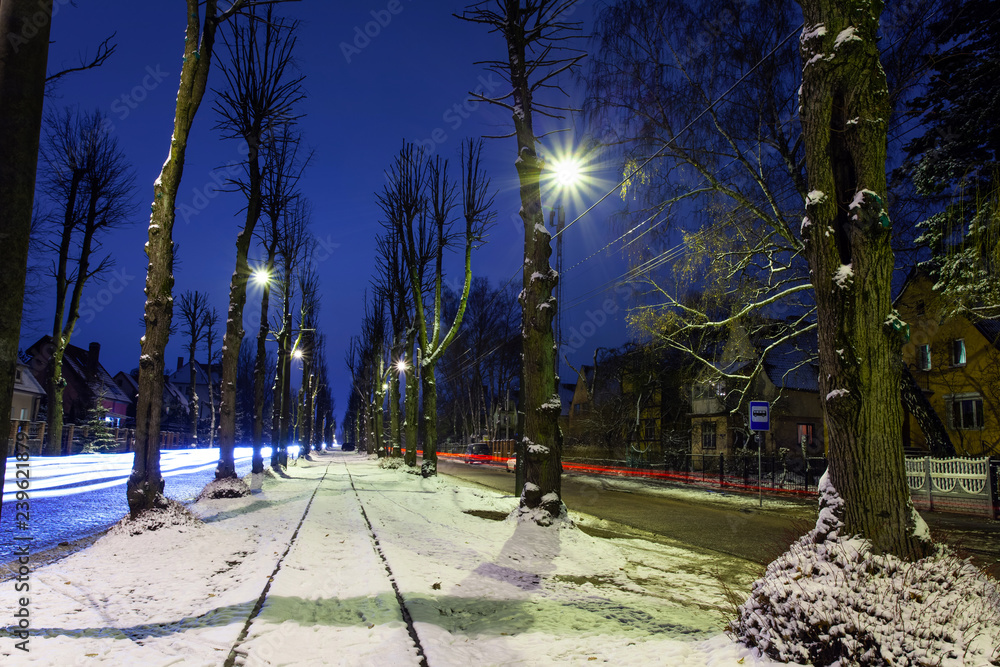 a small street of a night city with snowy tram tracks and traces of car headlights on a long exposure