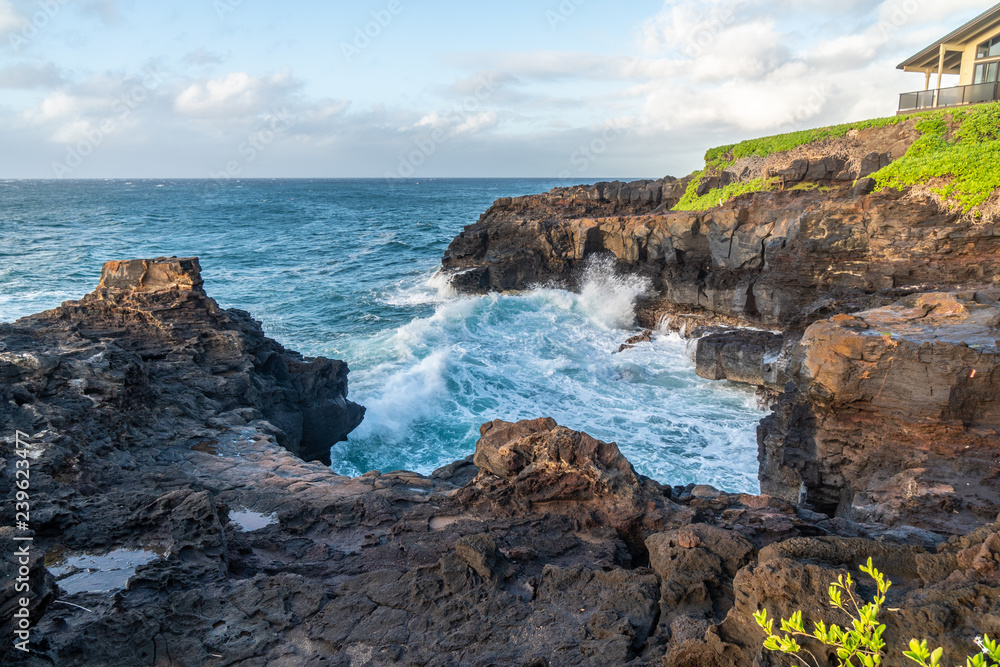 Ocean surf hitting the basalt cliff in a rock cove with building above, Kauai, Hawaii