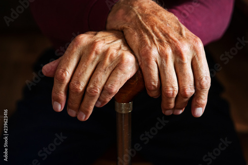 Old male hands on a wooden cane. Close-up.