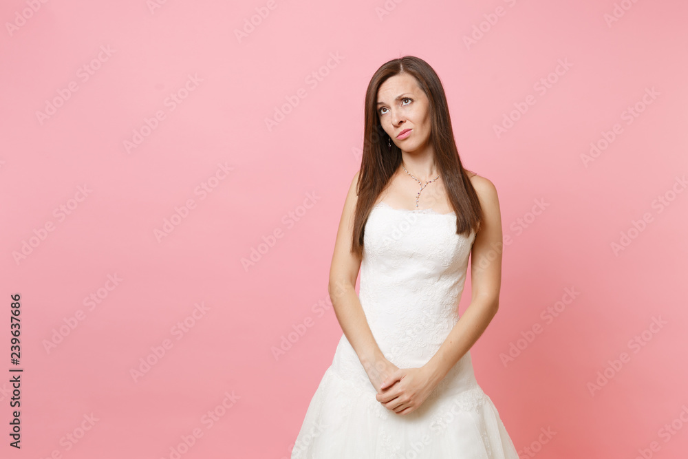 Portrait of concerned upset bride woman in white wedding dress standing holding hands crossed in front of her isolated on pink background. Wedding celebration concept. Copy space for advertisement.