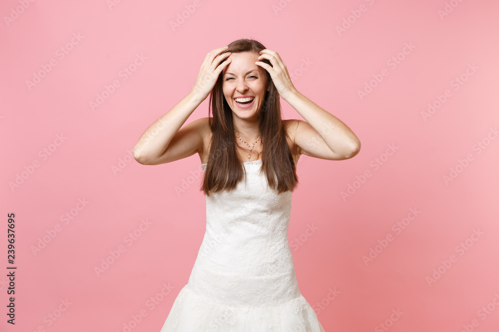 Portrait of joyful laughing bride woman in beautiful white wedding dress standing keeping hands near face isolated on pastel pink background. Wedding celebration concept. Copy space for advertisement. Portrait of joyful laughing bride woman in beautiful white wedding dress standing keeping hands near face isolated on pastel pink background. Wedding celebration concept. Copy space for advertisement.