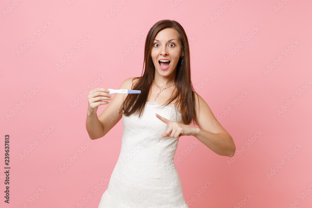 Amazed bride woman in white wedding dress pointing index finger on pregnancy test in hand isolated on pink background. Medical healthcare gynecological pregnancy fertility maternity people concept. Amazed bride woman in white wedding dress pointing index finger on pregnancy test in hand isolated on pink background. Medical healthcare gynecological pregnancy fertility maternity people concept.