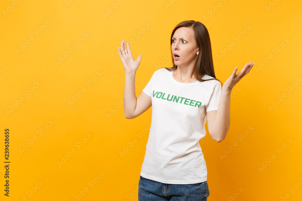 Portrait of scared shocked afraid young woman in white t-shirt with written inscription green title volunteer isolated on yellow background. Voluntary free assistance help, charity grace work concept. Portrait of scared shocked afraid young woman in white t-shirt with written inscription green title volunteer isolated on yellow background. Voluntary free assistance help, charity grace work concept.