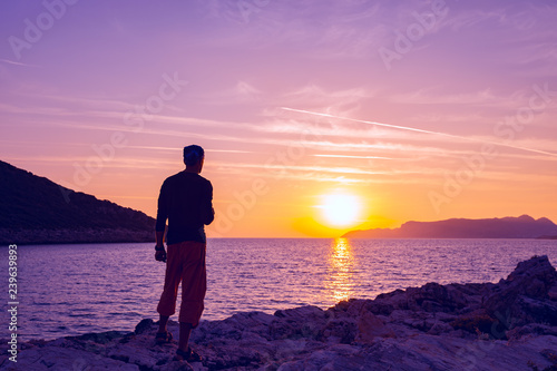 Silhouette of traveler who stands on the rock seashore