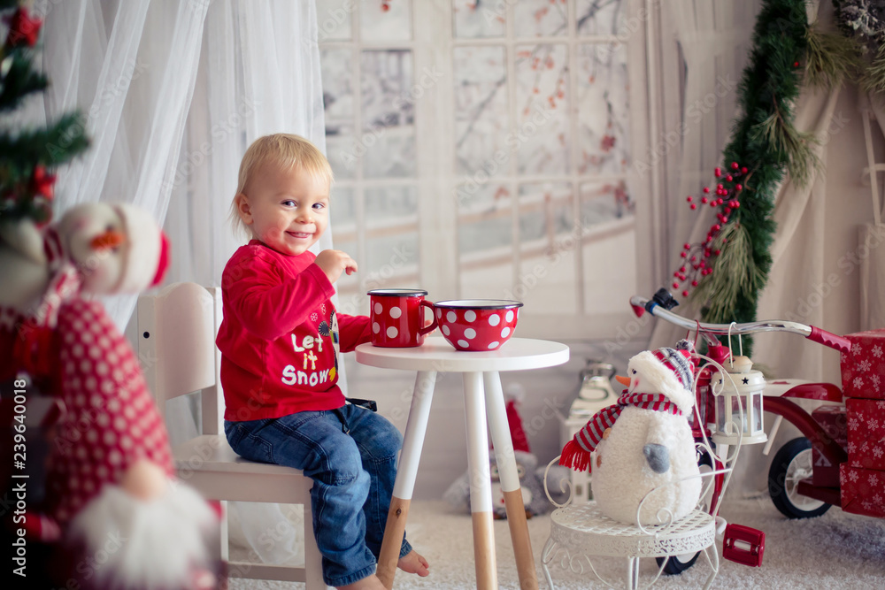 Naklejka premium Little toddler boy, drinking tea and eating cookies with plush toy on a snowy day