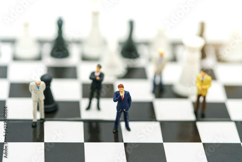Miniature people: Businessman handshake to business success on chessboard. Commitment, agreement, investment and partnership concept