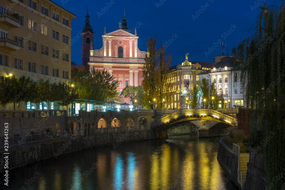 Fototapeta premium Night time view of the center of Ljubljana featuring the lit up pink Franciscan church and the three way bridge 