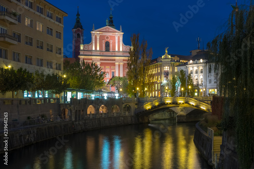 Night time view of the center of Ljubljana featuring the lit up pink Franciscan church and the three way bridge 