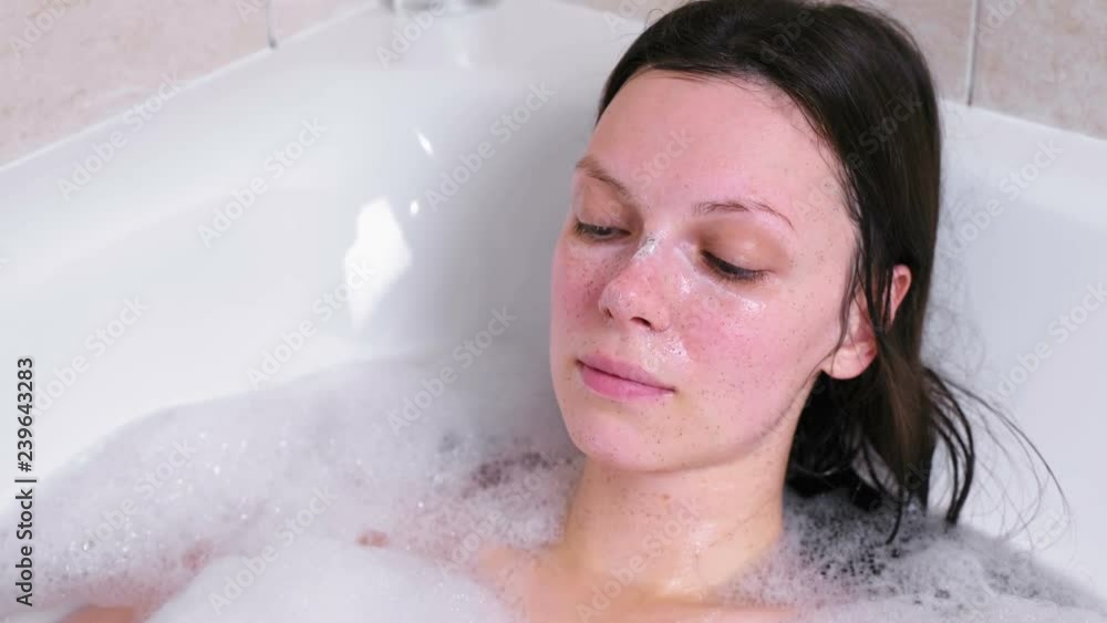 Woman washes her face with a sponge from a scrub lying in the bathroom. Woman washes her face with a sponge from a scrub lying in the bathroom.