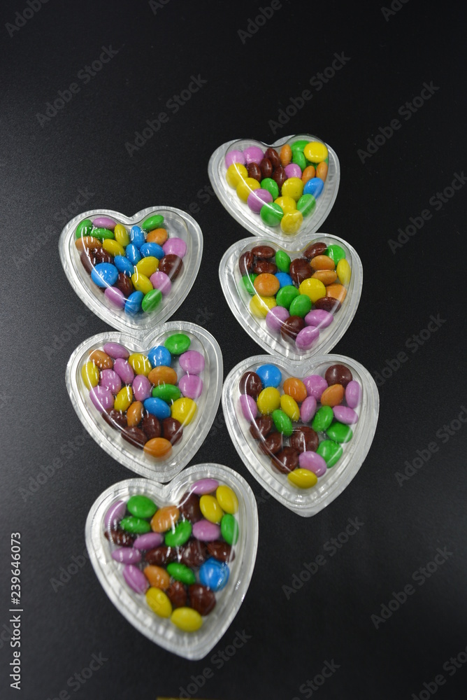 Very stylish combination of black background with silver boxes in the form of hearts and with multicolored chocolates in the middle of them, Valentine's Day, love and joy