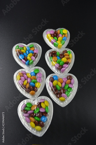 Very stylish combination of black background with silver boxes in the form of hearts and with multicolored chocolates in the middle of them, Valentine's Day, love and joy