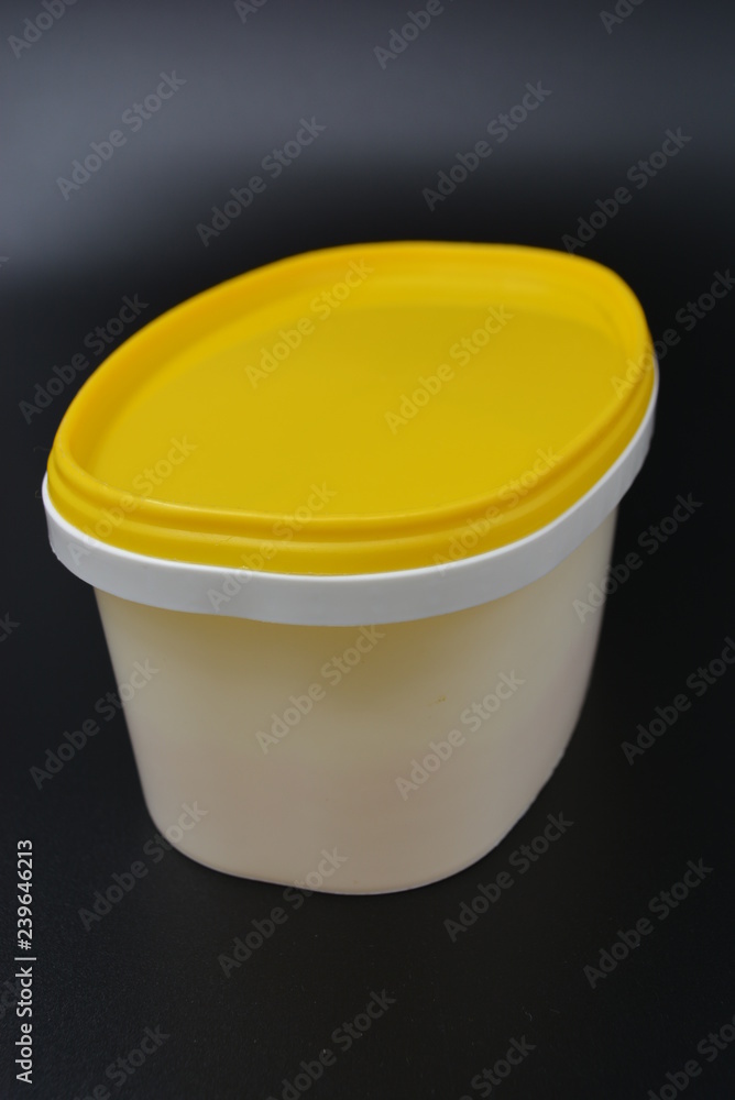 White plastic container for food and mayonnaise with a yellow cap on a black stylish background White plastic container for food and mayonnaise with a yellow cap on a black stylish background